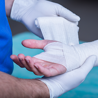 A close up image of a medical professional's gloved hands bandaging the hand and wrist of a patient.